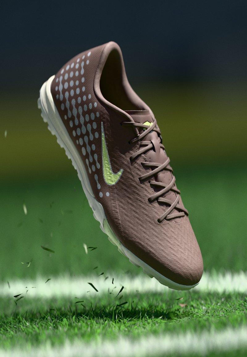 Καφέ αθλητικό παπούτσι με υφή στο πάνω μέρος, πράσινες λάιμ λεπτομέρειες και σχεδιασμό με σχέδιο. Διαθέτει λευκή σόλα και αιωρείται πάνω από γκαζόν.