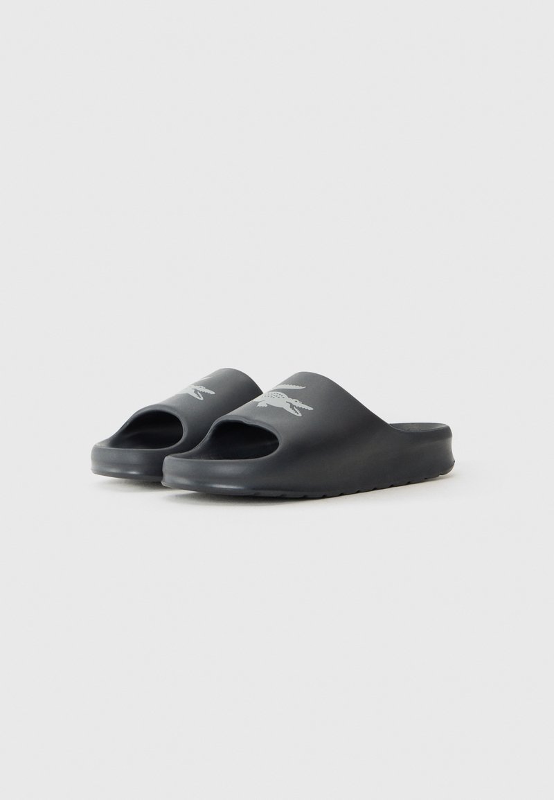 Des sandales noires en caoutchouc lisse, présentant un design ouvert à l'avant et un accent logo sur la sangle. Semelle texturée pour une meilleure adhérence.