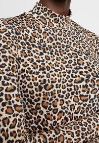 Topp med høy hals i leopardmønster laget av mykt stoff, med en blanding av brune, svarte og kremfargede nyanser, i en tettsittende design.