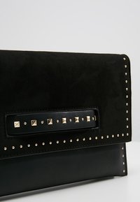 Zwarte leren en suède clutch met gouden piramide- en ronde studdetails langs de randen en uitsparing in de handgreep.