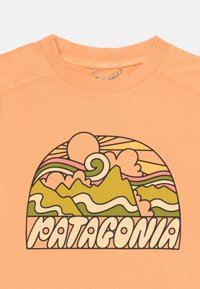 Perzikkleurig T-shirt met een retro grafiek van een berg en zonsondergang in groen, roze en wit. Tekst "PATAGONIA" in vetgedrukt, afgerond lettertype.