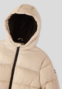 Beżowa kurtka puchowa z kapturem, z ciemnym, polarowym wykończeniem, zapinana na zamek błyskawiczny, o poziomym pikowanym wzorze. Małe logo na lewym rękawie.