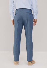 Pantaloni su misura di colore azzurro chiaro con un tessuto testurizzato, due tasche posteriori e una vita aderente, abbinati a scarpe beige senza lacci.