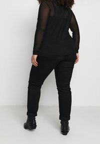 Haut à manches longues en mesh noir avec un motif à pois et un ourlet courbé, associé à un pantalon noir ajusté et des bottines.