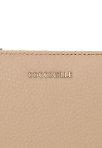 Portafoglio in cuoio marrone chiaro con superficie testurizzata, bordi cuciti e logo in oro goffrato "COCCINELLE" sulla parte anteriore.