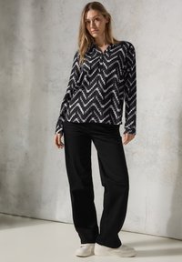 Camicia a maniche lunghe bianca e nera con motivo a zigzag, abbinata a pantaloni neri a vita alta e sneakers bianche.
