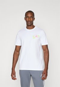Hvid bomulds T-shirt med et farverigt grafik på venstre bryst, rund hals design og korte ærmer. Glat tekstur, afslappet pasform.