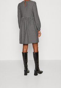 Svart och vit rutmönstrad långärmad klänning med insnävning i midjan, med en nyckelhålrygg och matchad med svart höga stövlar.