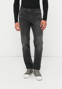 Mustad, kitsad teksad pleekinud viimistlusega, viie taskuga disainiga ja nupuga sulguriga. Sobitatud hallide tossudega, millel on valged tallad.