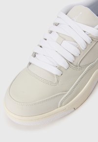 Lysebrune sneakers med en glat syntetisk overdel, hvide snørebånd, teksturerede sider og gummisål. Minimalistisk design med logo-detaljer.