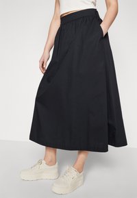 Falda negra hasta el tobillo hecha de tejido ligero, con una cinturilla elástica y bolsillos laterales, combinada con zapatillas de plataforma beige.