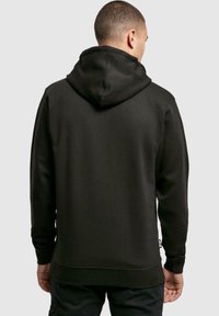 Black hooded sweatshirt with a relaxed fit, featuring a textured fabric, ribbed cuffs, and a small logo tag on the side.