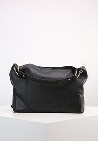 Black leather handbag with a slouchy design. Features silver chain accents and triangular sections at the base. Smooth texture, minimal detailing.