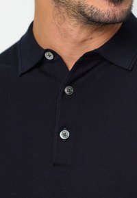 Marinblå polo t-shirt med krage, som har tre knappar och en ribbad struktur. Tyget verkar mjukt och åtsittande.