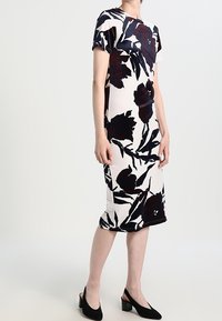 Sukienka w kwiatowy wzór z krótkimi rękawami, przedstawiająca ciemnoczerwone i czarne kwiaty na kremowym tle; długość do kolan i dopasowany krój.