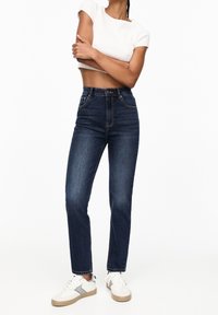 Jeans a vita alta, a gamba dritta in denim blu scuro con cuciture chiare, dotati di tasche frontali e chiusura con zip classica.