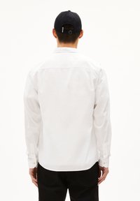 Witte langslib shirt met een button-down kraag en manchetten, gemaakt van een gladde stof. In combinatie met donkere broek. Achteraanzicht.