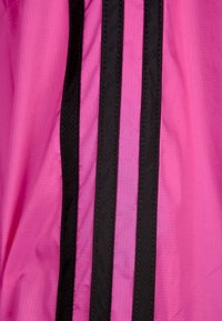 Tela ligera de color rosa con tres franjas verticales negras. La textura presenta un sutil patrón de cuadrícula, con costuras duraderas a lo largo de los bordes.