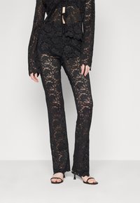 Svart spets långärmad topp och byxor i set med blommönster, med en knytning fram och något utsvängda ben. Bärs med svarta klacksandaler.