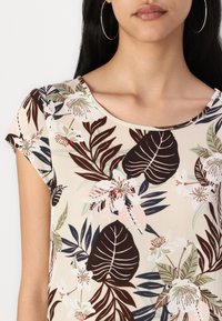 T-shirt à manches courtes avec une base crème ornée de motifs floraux sombres, comprenant des feuilles et des fleurs dans des tons de vert, rose et marron.