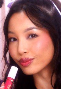 Close-up van een persoon die een roze lipproduct vasthoudt met een glanzende finish. De lippen zijn glanzend en vol, aangevuld met een subtiele blos en een gladde huid.