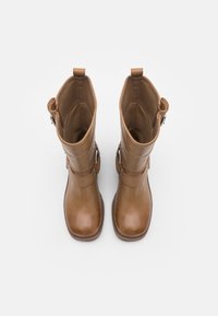 Par av bruna läderstövlar i midikniv, med fyrkantiga tår, sidoband och dragöglor högst upp mot en vit bakgrund.