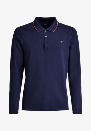 Polo à manches longues bleu marine avec trois boutons, bordure rouge et blanche sur le col, et petit logo triangulaire Guess sur la poitrine.
