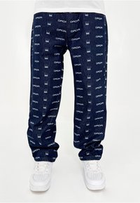 Pantalons en denim bleu marine avec des logos blancs répétés "DADA" et des motifs de couronne. Coupe ample avec poches latérales et poignets élastiques.