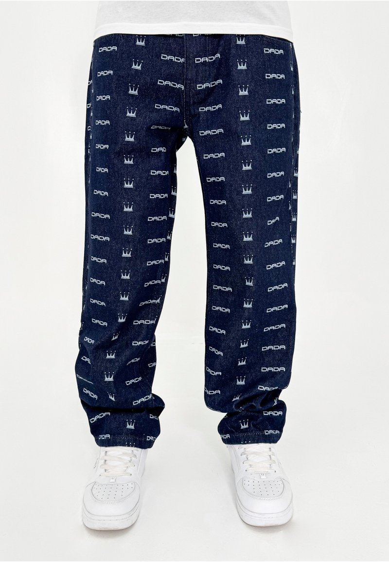 Pantalons en denim bleu marine avec des logos blancs répétés "DADA" et des motifs de couronne. Coupe ample avec poches latérales et poignets élastiques.