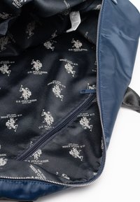 Navy blue textile bag interior with a zipper; U.S. Polo Assn. logo pattern in white on a dark background. Smooth material texture.