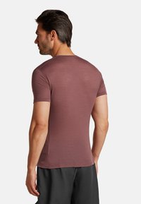 T-shirt a maniche corte di colore bordeaux con una superficie a trama. Presenta un colletto rotondo e un design aderente, abbinato a pantaloni corti scuri.
