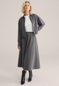 Grå tygjacka och matchande kjol med en kedjebälte-detalj, tillsammans med en vit topp och svarta ankelstövlar. Slät textur genom hela plagget.