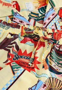 Pijamale galbene cu modele cu desene animate cu crabi, bărci și mâncare. Țesătura are o textură netedă și o talie elastică.