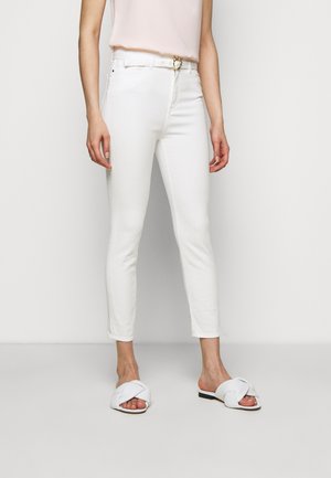 Witte skinny jeans met een hoge taille en een gouden cirkel-beltbuckle. Gecombineerd met witte instapsandalen met een geknotte bandontwerp.