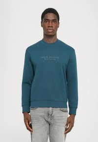 Tyrkisk bomullssweatshirt med rund hals, ribbede mansjetter og hem. Har fronttekst "ARMANI EXCHANGE MILANO/NEW YORK" i kontrastfarge.