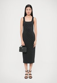 Zwart gebreide jurk met een patroon waarin de letter "M" voorkomt. Gecombineerd met een zwarte handtas en zwarte sandalen met bandjes. Gladde textuur.