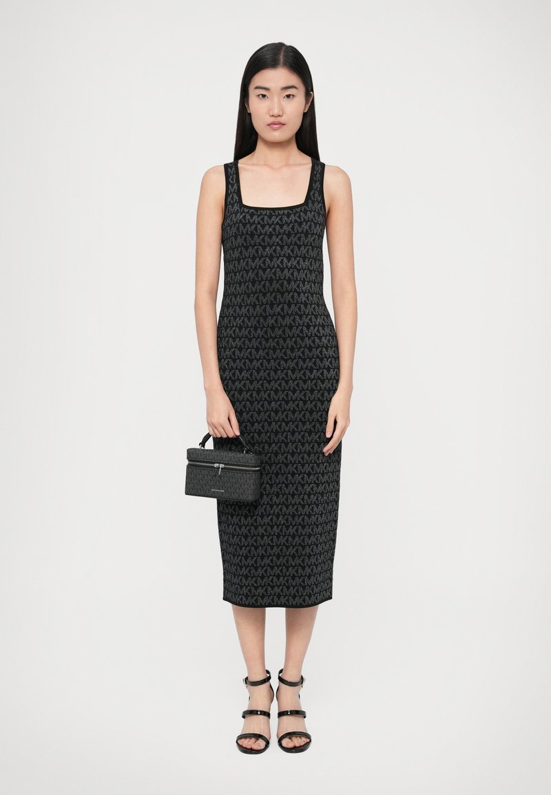 Zwart gebreide jurk met een patroon waarin de letter "M" voorkomt. Gecombineerd met een zwarte handtas en zwarte sandalen met bandjes. Gladde textuur.