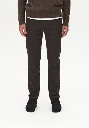 Hnědé, slim-fit kalhoty vyrobené z texturované tkaniny s hladkým povrchem. Spárované s černou obuví a hnědým svetrem, čímž vytvářejí soudržný vzhled.