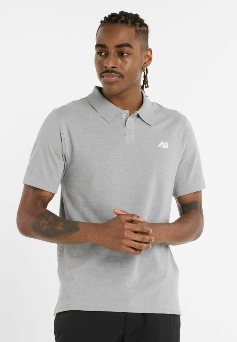 Polo gris de manga corta con cuello clásico y tres botones, que presenta un pequeño logotipo blanco en el lado izquierdo del pecho. Tela de algodón suave.