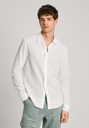 Camisa blanca de manga larga hecha de un tejido ligero, con un diseño de botones, cuello y sutiles detalles de costura.