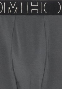 Boxer briefs in tessuto elasticizzato grigio con una cintura elastica nera che presenta testo bianco. Texture liscia e design aderente per il comfort.