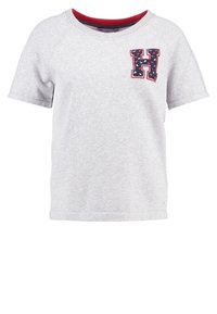 Grå t-shirt med kort ärm gjord av mjukt tyg. Har en röd, ribbad halsringning och en marineblå broderad "H"-logotyp på vänster bröst.