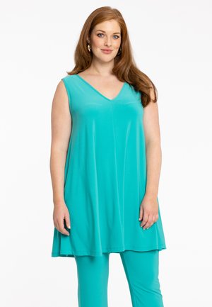 Een mouwloze tuniek in helder turquoise, met een V-halsontwerp en een vloeiende silhouet, gecombineerd met bijpassende strakke broeken. Zachte stoffen textuur.