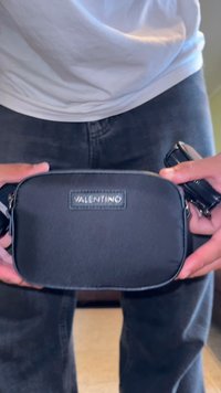 Borsa in tessuto nero a forma rettangolare, con una toppa del logo Valentino, chiusura con zip e tracolla regolabile. Tessuto liscio.