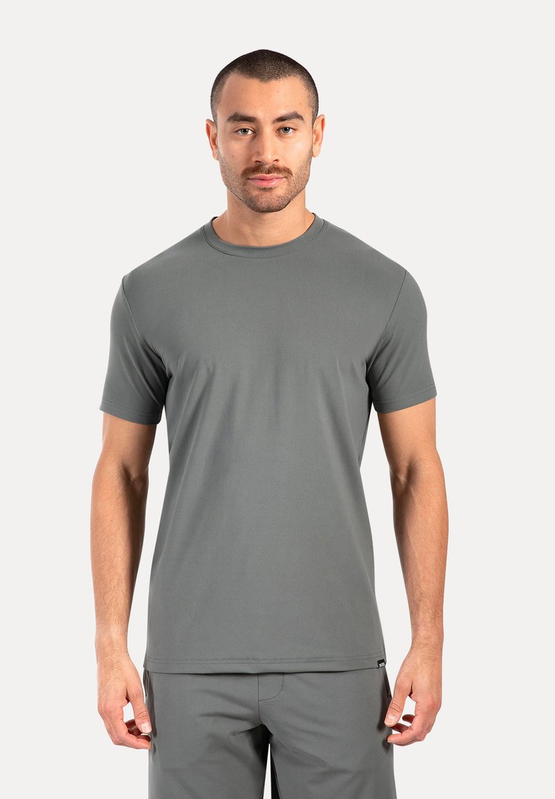 Camiseta de manga corta y cuello redondo en tejido gris oscuro. Textura suave, diseño ajustado y marca mínima. Combinada con pantalones a juego.