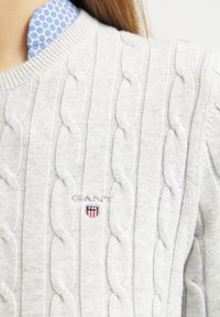 Maglione grigio a maglia con trama a coste e piccolo logo GANT sul petto, indossato sopra una camicia con colletto a pois blu.