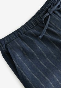 Pantaloni a strisce blu navy realizzati in tessuto morbido con vita elasticizzata e cordoncino. Presentano sottili strisce verticali di colore chiaro.
