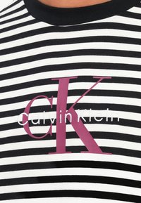 Juodai baltos dryžuotos marškinėlių su apvalia kaklo iškirpte, išryškėjusiu raudonu logotipu "CK" ir "Calvin Klein" tekstu balta siuvinėta.