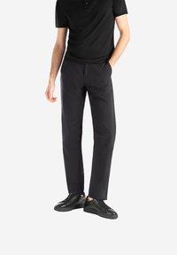 Polo nero abbinato a pantaloni neri su misura e sneakers nere. I pantaloni hanno una texture liscia e un design a gamba dritta.