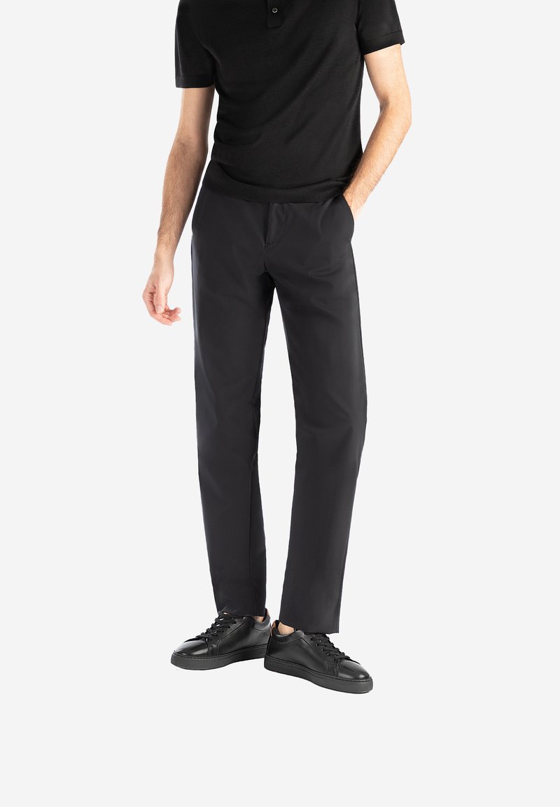 Polo nero abbinato a pantaloni neri su misura e sneakers nere. I pantaloni hanno una texture liscia e un design a gamba dritta.